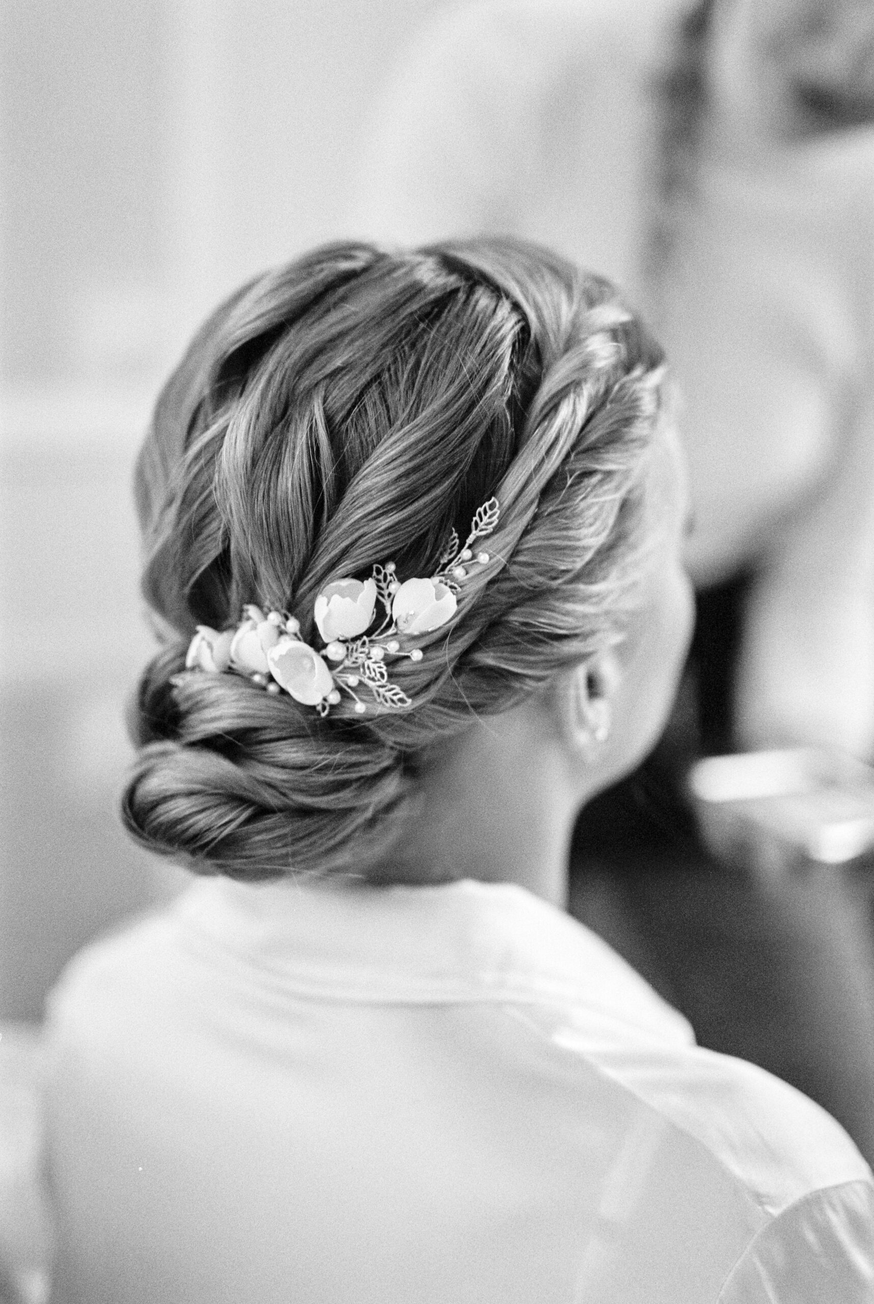 Black and white photo of an elegant bridal updo hairstyle with floral accessory.