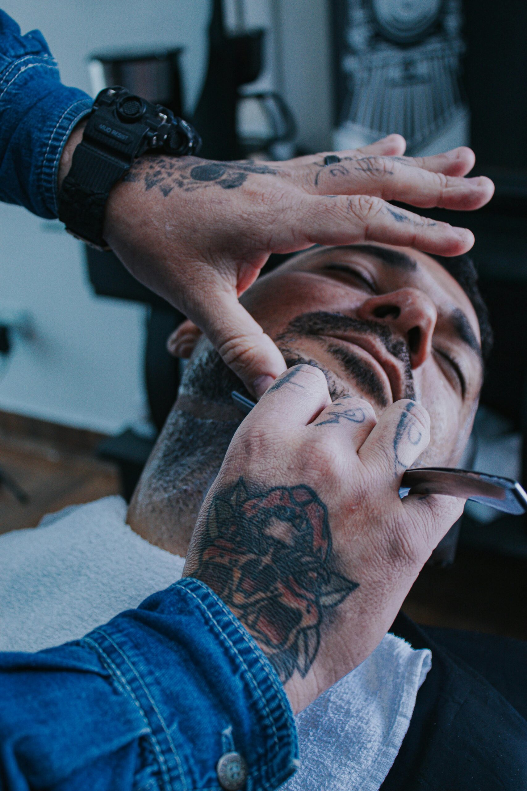 Barber expertly trims a client's beard with a straight razor while he relaxes.