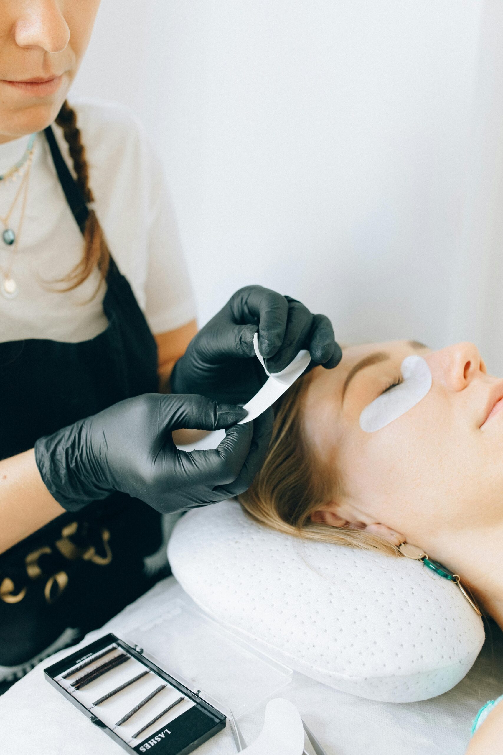 Professional applying eyelash extensions on a young woman in a beauty salon.