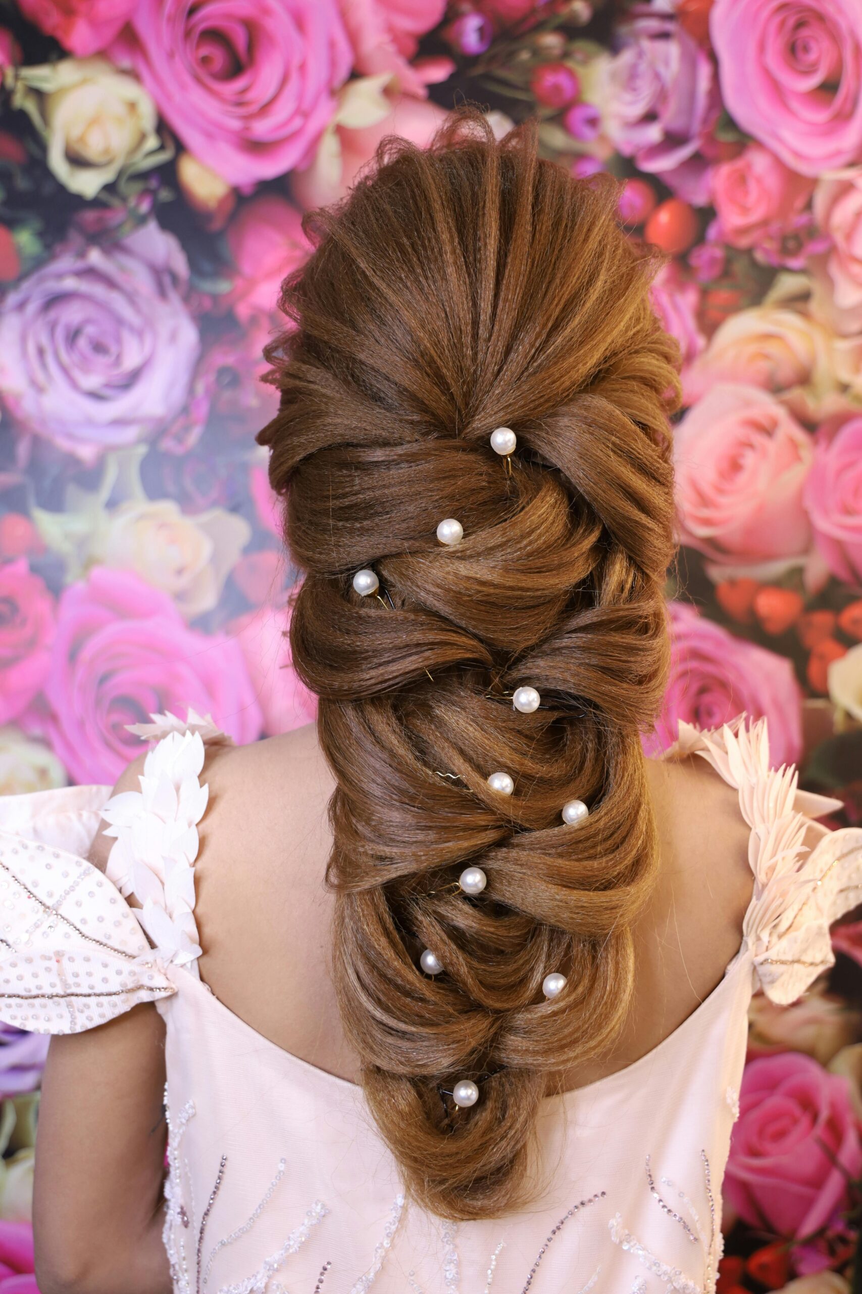 Back view of unrecognizable lady in pink dress with hairdo and head accessories near wallpapers covered with roses