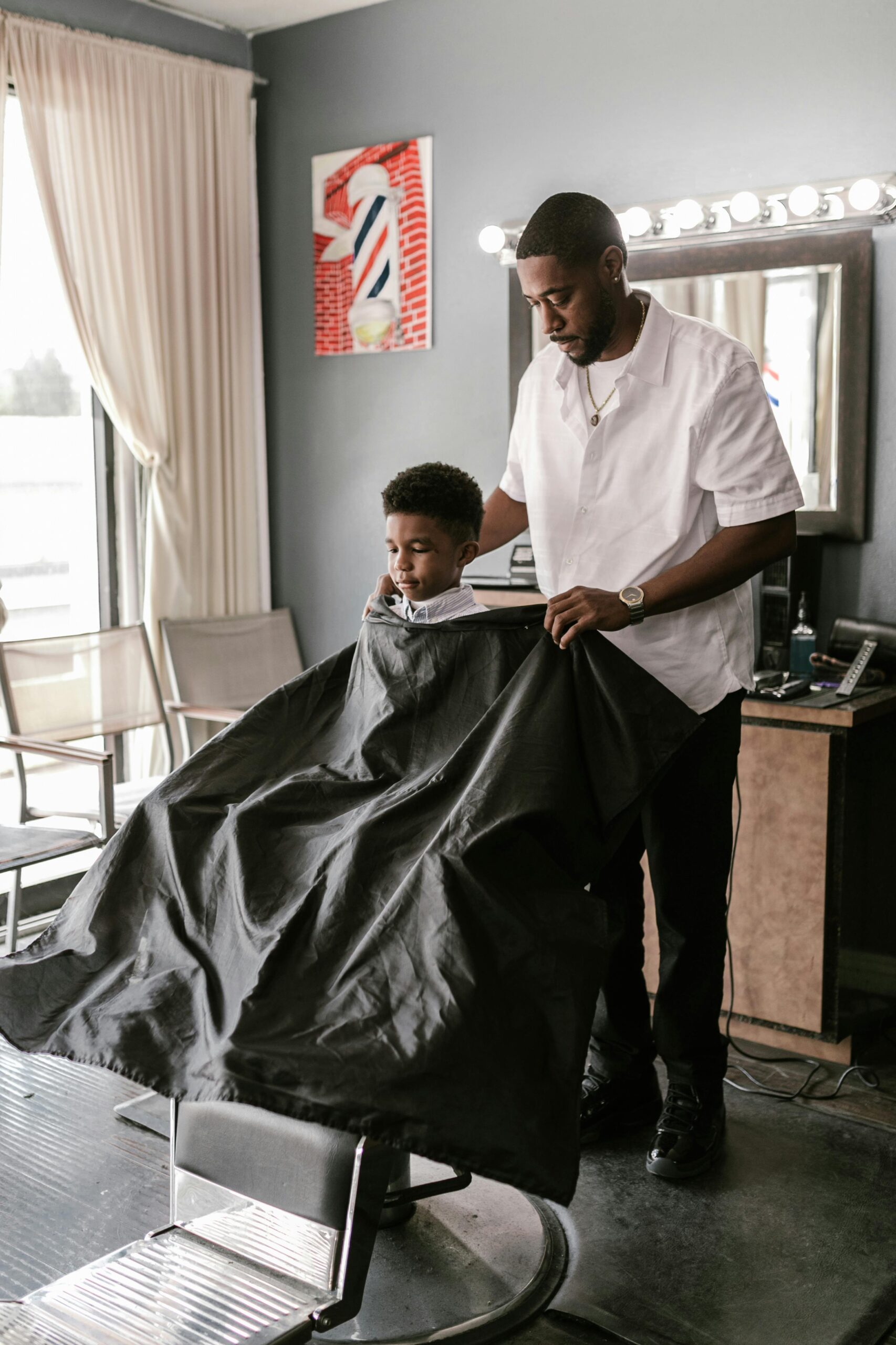 A barber drapes a cape over a young boy in a barber shop, preparing for a haircut.