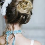 Back view of an elegant updo hairstyle adorned with feathers, perfect for bridal fashion.