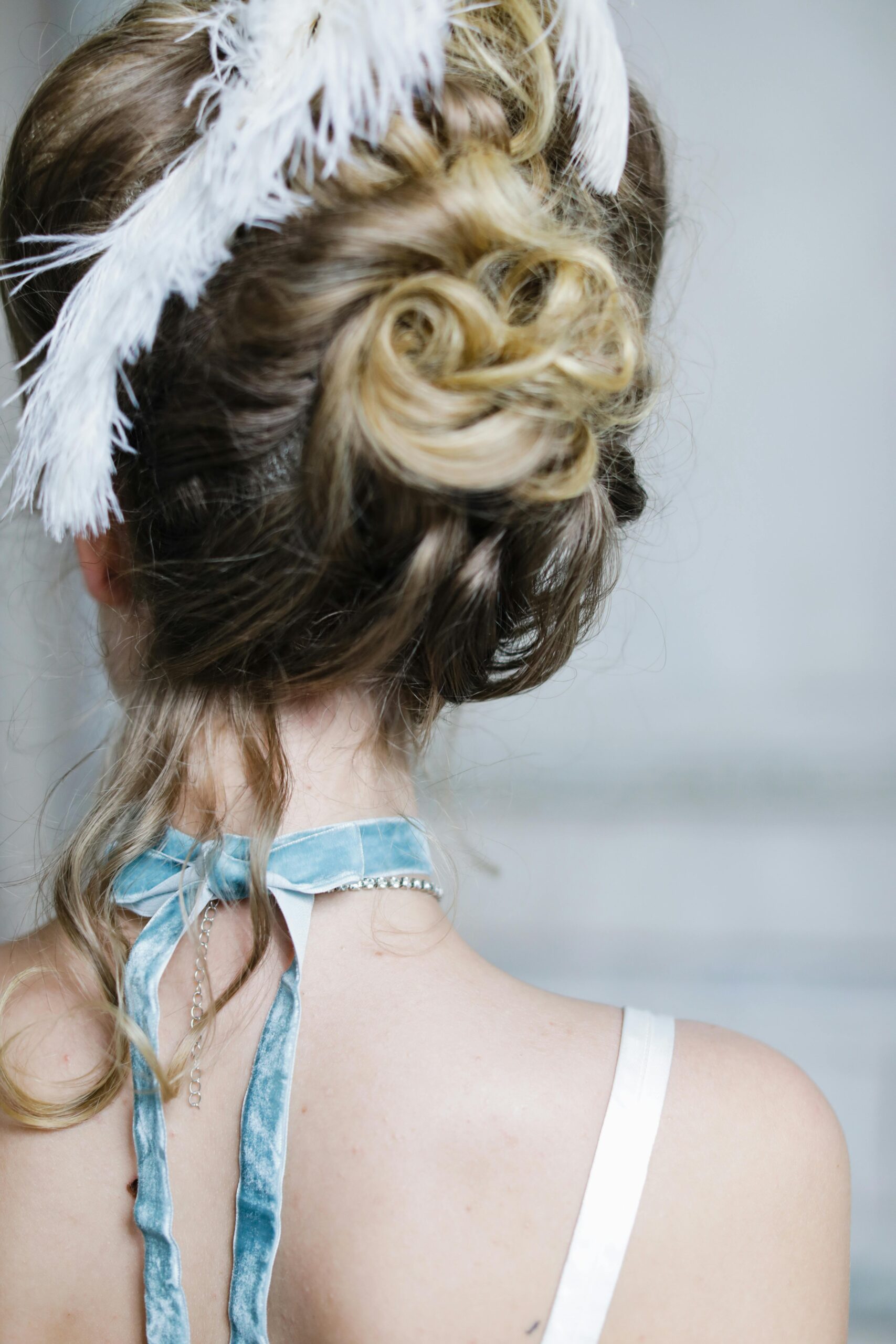 Back view of an elegant updo hairstyle adorned with feathers, perfect for bridal fashion.